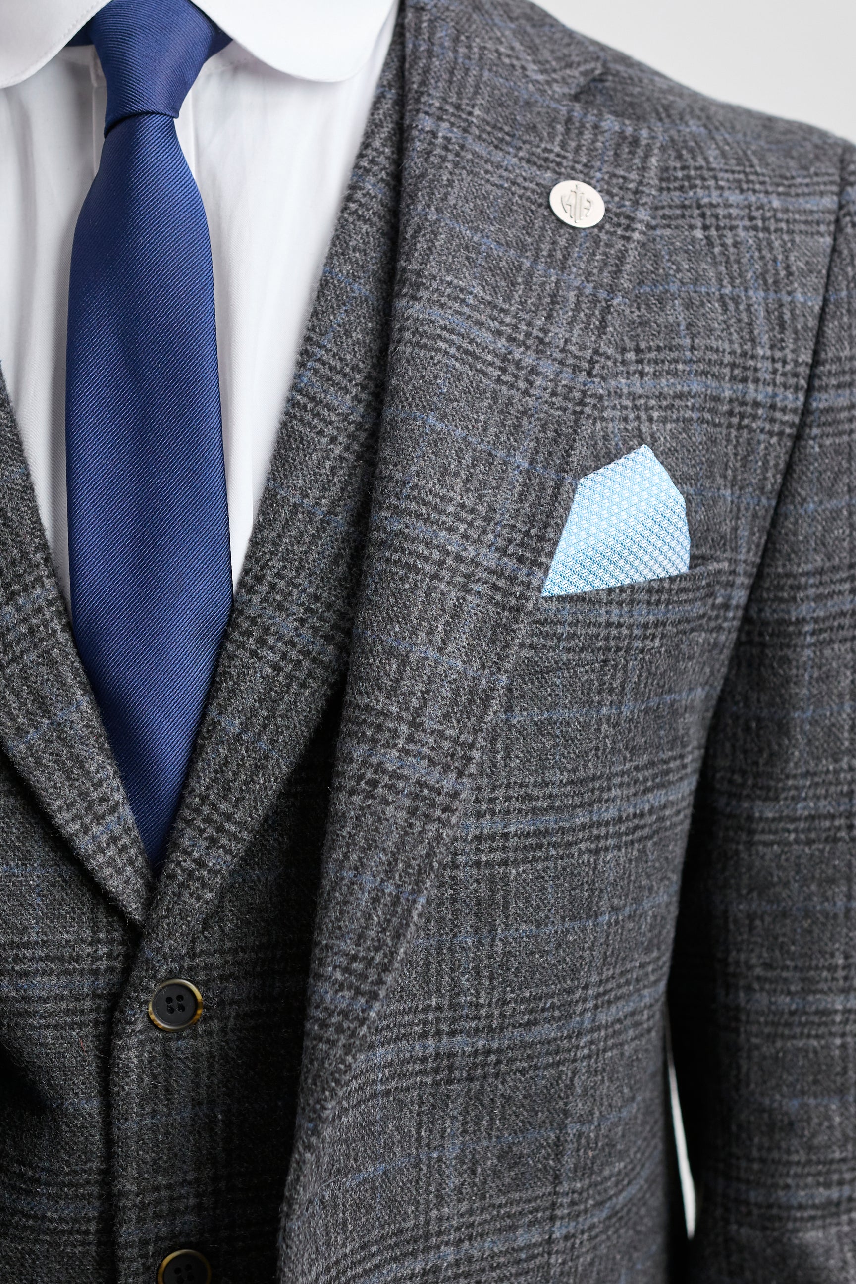 Gray checkered suit with blue tie and pocket square on a light gray background
