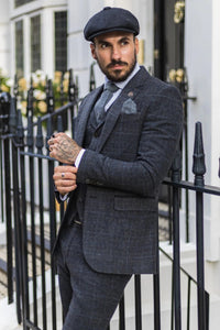 Man in a gray checkered suit standing outdoors next to a black metal gate.