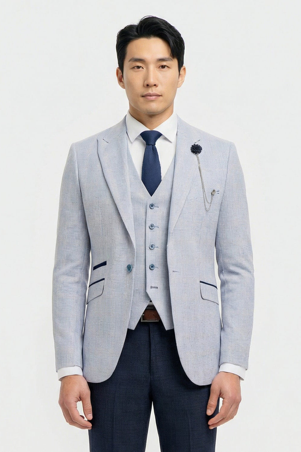Mann mit hellgrauem Blazer, marineblauer Weste und dunkelblauer Krawatte vor weißem Hintergrund