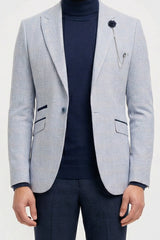 Mann mit hellgrauem Blazer, dunkelblauem Rollkragenpullover und dunkler Hose vor weißem Hintergrund
