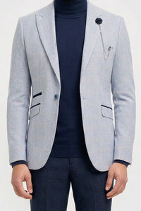 Mann mit hellgrauem Blazer, dunkelblauem Rollkragenpullover und dunkler Hose vor weißem Hintergrund