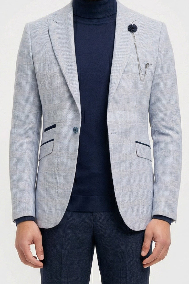 Mann mit hellgrauem Blazer, dunkelblauem Rollkragenpullover und dunkler Hose vor weißem Hintergrund